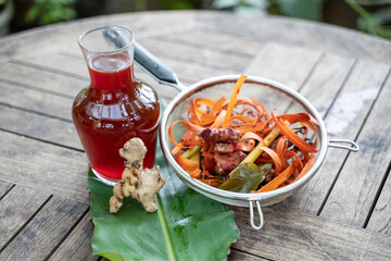 wedang uwuh drinks in glass bottles and red ginger, secang wood shavings, lemongrass in stainless sieve, heritage of traditional Javanese traditional Indonesian medicine