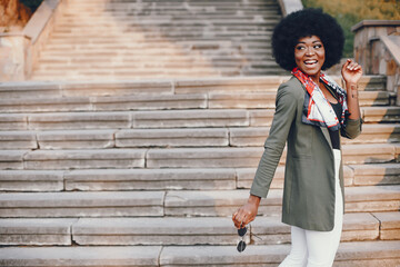 Fashionable girl in a summer city. Black lady in a green jacket. Woman in a red scarf. Famale with sunglasses