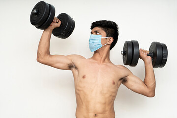 Fototapeta na wymiar Fitness man with mask for epidemic protection working exercise for arm,biceps, and shoulders with dumbbells.Training in epidemic time