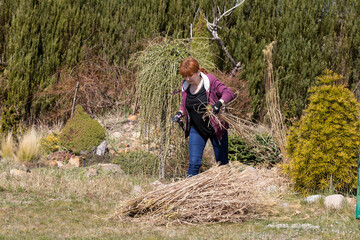 The red-haired woman lifts the cut dry grass onto a pile of straw deposited on the lawn.