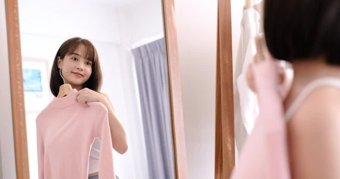 Asian woman choosing clothes dress-up closet collection mirror at home