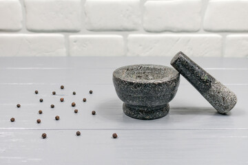 Granite gray mortar with pestle on a gray wooden table background on a white brick wall background. Stone mortar is an important tool in cooking pepper food.