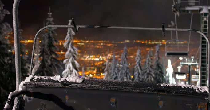 Zoom in time lapse shot of snow on ski lift against illuminated city at night - Vancouver, Canada