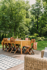 Dining table covered with orange tablecloth standing on wooden terrace in green garden