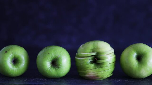 green apples lined up on wooden table with centered one cut into slices and camera panning