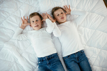 Brothers making silly faces in bed. Young boys having fun in bedroom.