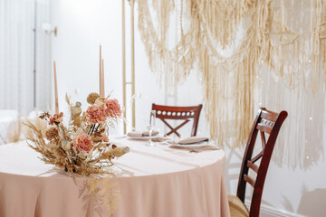 Romantic table setting in a restaurant for a holiday. Wedding decor for newlyweds at a banquet. Dried flowers floristry and candles, boho style. Cartering service for the bride and groom and guests.