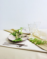 Obraz na płótnie Canvas table setting details. beige plates and cutlery on a table with a decor of green leaves of mountain ash. served table in the interior.