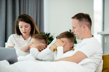 Obraz premium Young family watching movie on lap top. Beautiful parents with kids enjoying at home.