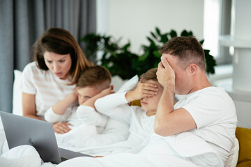 Obraz premium Young family watching movie on lap top. Beautiful parents with kids enjoying at home.