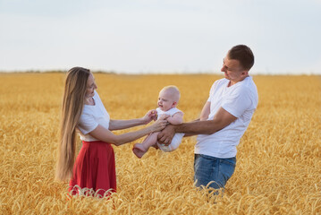 Young couple with small child walks through wheat field. Happy parenthood. Parents and child outdoors