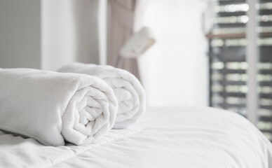 Fototapeta na wymiar Roll of white clean bath towels on the bed in hotel room. Copy space.