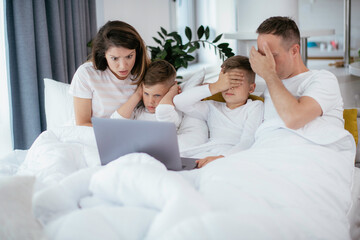 Obraz premium Beautiful parents with kids enjoying at home. Young family watching movie on lap top.