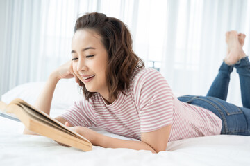 Obraz premium An Asian woman is lying reading in bed with a kitten. concept life style, pets, stay at home, new normal, mental state, interior decoration, background
