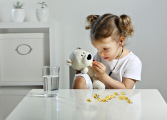 A glass of water and fish oil pills. A child plays doctor with bear cub, takes omega 3 pills.