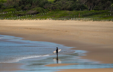 Fototapeta na wymiar Silohette surfer walking on beach with her surfboard under her arm, no one else around