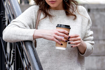 young girl leans on the railing and holds paper сup of coffee to take away