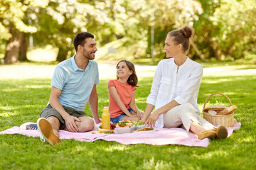 family, leisure and people concept - happy mother, father and daughter having picnic at summer park