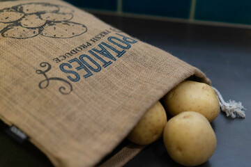 Fresh potatoes from the local market in a brown sack on grey kitchen bench. Reusable burlap sack bag for keeping potatoes fresh.