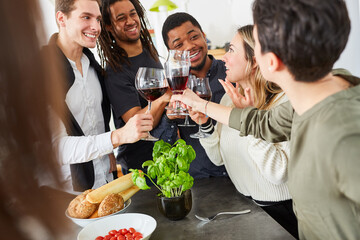 Gruppe junger Leute in WG beim Anstoßen mit Glas Wein