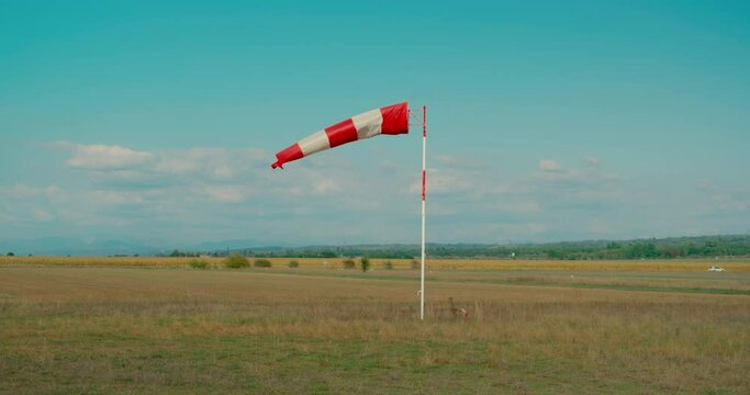 Cinematic symmetrical shot of small airport for private jets. Windsock blow in wind to show speed and direction of wind gusts. Summer vibes in rural France, blue skies, perfect day for flying