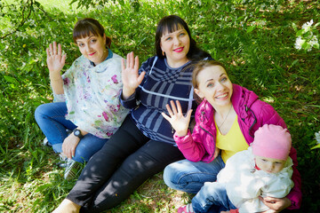 Three different funny women and one small seriously girl in the park full of apple blossom trees in a spring day. Aunts and niece in nature landscape