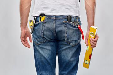 repair, construction and building - male worker or builder with level and working tools in back pockets over grey background