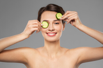 beauty, skin care and detox concept - beautiful woman making eye mask of cucumbers over grey background
