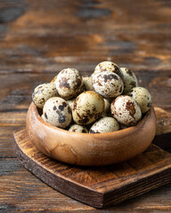 Fresh quail eggs in a wooden bowl on a brown wooden table. Raw quail eggs close-up on a culinary...