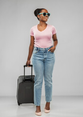 travel, tourism and vacation concept - happy african american young woman in sunglasses with carry-on bag over grey background