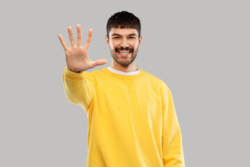 gesture, count and people concept - happy smiling young man in yellow sweatshirt showing his hand...