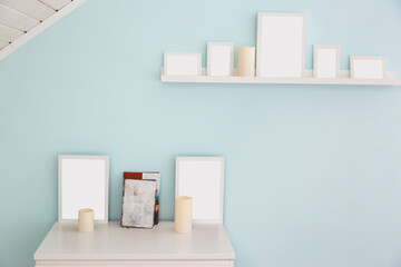 a white shelf and a table with white frames for photos, beige candles and books in the attic room. light blue wall. high key