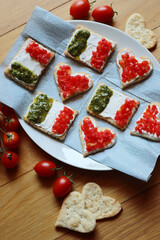 Salad cookies in shape of red heart and italian flag on a plate on wooden table. Snack with tradional  italian ingredient: pesto, cheese and red tomatoes.
