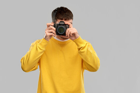 photography and people concept - young male photographer in yellow sweatshirt taking picture with digital camera over grey background