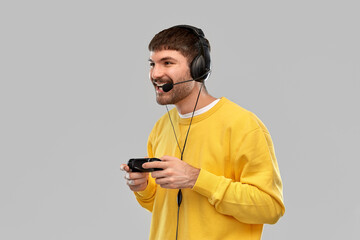 technology, gaming and people concept - happy smiling young man or gamer in headphones with gamepad playing and streaming video game over grey background © Syda Productions