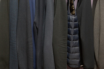 Close-up of men's shirts, jackets and sweaters of different calm dark colors hanging in a row. background, abstraction,