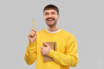 inspiration, idea and people concept - smiling young man in yellow sweatshirt with diary and pencil over grey background