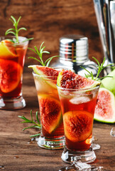 Red cocktail with cognac, liquor, lime juice, figs and honey, old wooden table, bar tools, copy space