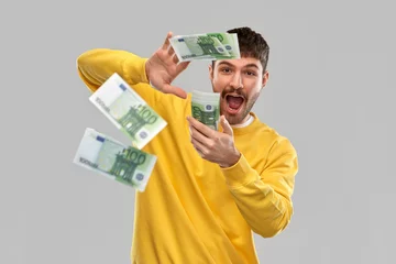 Fotobehang people concept - happy young man in yellow sweatshirt pouring money over grey background © Syda Productions