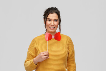 party props, photo booth and people concept - portrait of happy smiling young woman with pierced nose big red bowtie over grey background © Syda Productions