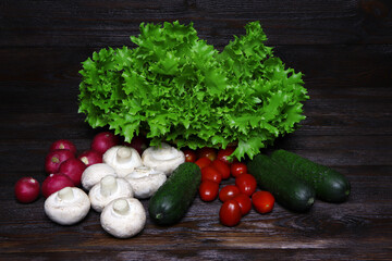Fresh vegetables on a wooden background. A green salad, radishes, mushrooms, cucumbers and tomatoes on a table. Rustic style. Vegetarian food. Raw, organic vegetables.
