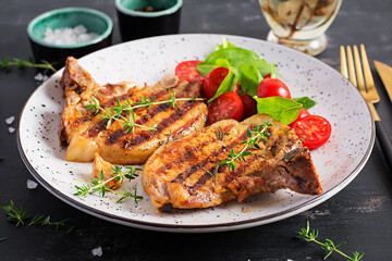 Grilled pork steaks and salad with tomatoes in plate on dark background.