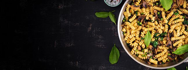 Fusilli pasta with spinach and mushrooms on a pan. Vegetarian / vegan  food. Italian cuisine. Top view, banner, copy space