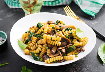 Fusilli pasta with spinach and mushrooms on a white plate. Vegetarian / vegan  food. Italian cuisine.