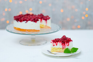 Cake with raspberries standing on a cake plate on the background of lights and a piece of cake lying nearby