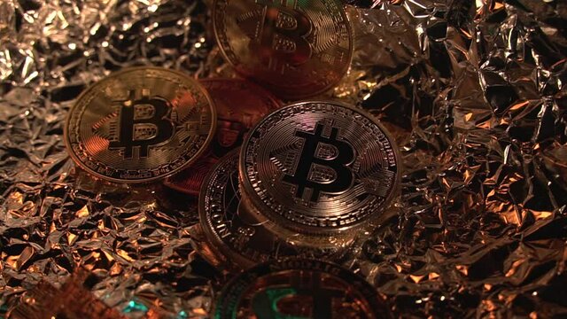 Many golden Bitcoin rotate on reflect surface. Light illuminates them. Digital coin. Virtual currency. New money