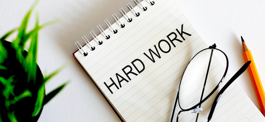 Keyword HARD WORK - business concept text on a white notebook and glasses, pencil , green flowers