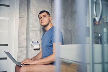 Naklejka na ściany i meble Young man with laptop on a toilet