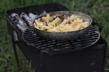 jacket potatoes, squash and sausages are cooked in a large frying pan on an open fire