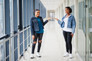 Two african woman friends in jeans jacket show hands indoor together.